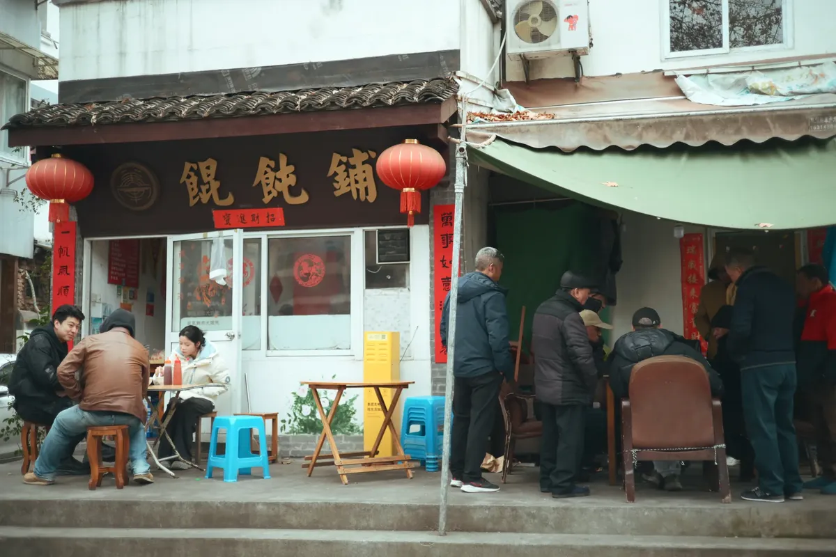 赤い灯りとサインが見える伝統的な中国レストランの外れで、人々が集まって交流している