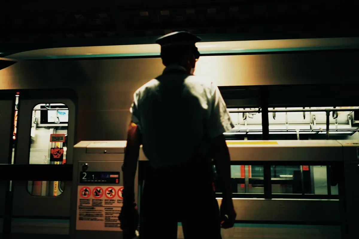 Silhouetted station worker at a subway platform during night, overseeing train arrival.